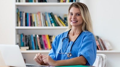 Nurse smiling while sitting at a laptop, engaged in coursework for an online MSN program.