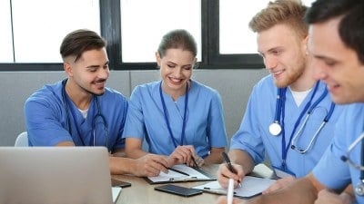 Group of nurses sitting at a table discussing patient care during a meeting while enrolled in one of the cheapest online DNP programs