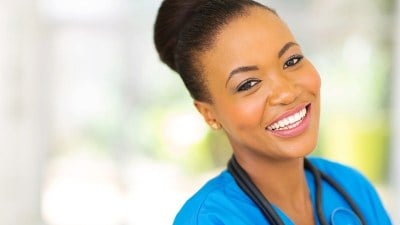 Smiling medical assistant in blue scrubs standing in a bright healthcare facility in California.